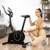 A woman is adjusting the seat of a stationary exercise bike in a home gym setting. Náhľad obrázku produktu