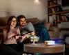A couple playing video games projected from a mini projector. Produktbild-Vorschau