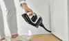 A person is using a handheld vacuum cleaner to clean a corner. Produktbild-Vorschau