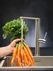A hand holding a bunch of carrots under a running faucet in a sink. Produktbild-Vorschau