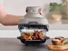 A hand is holding the top handle of a Ninja CRISPi air fryer, which is open and cooking food in a glass dish. Anteprima dell’immagine prodotto