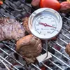A close-up of a grill thermometer placed on a grill with meat cooking. Produktbild-Vorschau