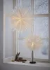 Two white star-shaped lamps are placed on a windowsill with a snowy winter scene visible through the window. Podgląd zdjęcia produktu
