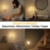 A collage of four images showing LED night lights plugged into wall sockets in various home settings, including a nursery, bathroom, bedroom, and staircase. Náhled obrázku produktu