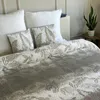 A bed with a quilt and pillows, with a plant on a side table. Náhľad obrázku produktu