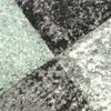 A close-up view of a carpet with an abstract checkered pattern in shades of green, gray, and anthracite. Produktbild-Vorschau