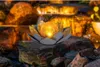 A solar-powered lotus-shaped light sits on rocks near a waterfall. Produktbild-Vorschau