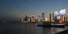 A city skyline at dusk with illuminated buildings and a body of water in the foreground. Anteprima dell’immagine prodotto