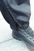 A close-up of a person's leg wearing black pants with a zipper and a black boot. Náhled obrázku produktu