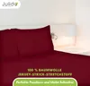 A close-up view of a burgundy bed sheet and pillow, with a bedside lamp and wall light in the background. Produktbild-Vorschau