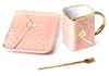 A pink ceramic mug, saucer, and spoon set with gold accents, displayed on a white background. Produktbild-Vorschau