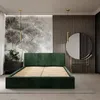 A bedroom scene featuring a green upholstered bed frame with a slatted base, a bedside table with flowers, and a decorative round mirror. Náhled obrázku produktu