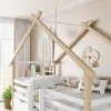 A close-up view of a white wooden house-shaped bunk bed frame with wooden beams and bedding. Voir les images du produit
