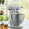 A white KitchenAid stand mixer is shown on a countertop with two cupcakes in the foreground. Produktbild-Vorschau