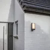 A close-up view of an exterior LED wall light mounted on a white brick wall next to a door and window. Anteprima dell’immagine prodotto