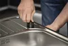 A person's hands are shown installing a part onto a stainless steel sink. Produktbild-Vorschau
