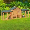 A wooden rabbit hutch with multiple levels and compartments, set up on a green lawn in a garden with lush foliage in the background. Anteprima dell’immagine prodotto