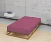 A bed frame with a pink mattress in a minimalist room with a concrete wall and a floating shelf. Produktbild-Vorschau