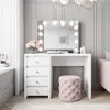 A white vanity table with a lighted mirror, drawers, and a pink stool in a room. Produktbild-Vorschau