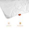 A close-up of a white duvet with a small orange tag and two informational icons below. Voir les images du produit