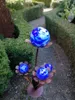A garden decoration with blue and white glass spheres on metal stems resembling flowers, set in a garden path with trimmed hedges. Anteprima dell’immagine prodotto