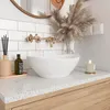 A modern bathroom vanity with a white vessel sink, brass faucet, and decorative elements. Anteprima dell’immagine prodotto