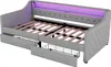 A grey upholstered daybed with wooden slats and two pull-out drawers, one of which is open, revealing a wire basket. Purple LED lighting is visible along the headboard. Produktbild-Vorschau
