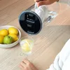A person is pouring water from a filter jug into a glass with a lemon slice. A bowl of lemons and a green apple are visible on the side. Produktbild-Vorschau