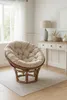 A papasan chair with a beige cushion sits on a light gray rug in a well-lit room with a window and a console table. Produktbild-Vorschau