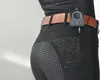 Close-up of the lower body of a person wearing black riding pants with a brown belt and a black device attached to the belt. Náhľad obrázku produktu