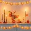 A festive Halloween or Thanksgiving decoration featuring string lights with maple leaf and pumpkin motifs, candles, and a floral arrangement on a mantelpiece. Náhled obrázku produktu