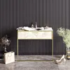 A modern console table with a marble-effect top and gold frame, set against a dark, ribbed wall. Decorative items like a globe, books, and perfume bottles are placed on top, and high heels are on the floor next to it. Produktbild-Vorschau