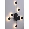 A black, modern wall lamp with multiple circular lights is mounted on a light gray wall. Produktbild-Vorschau
