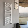 A white towel radiator is mounted on a gray wall in a modern bathroom with a large window overlooking a landscape. Produktbild-Vorschau