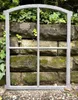 A gray metal window frame is placed in front of a stone wall covered in moss and ivy. Produktbild-Vorschau