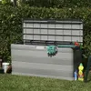 A grey garden storage box with the lid open, placed on a lawn in front of a hedge. Gardening tools and supplies are visible around the box. Produktbild-Vorschau