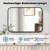 A rectangular bathroom mirror is displayed on a wall above a cabinet. The mirror reflects a room with a window and artwork. Below the mirror are three icons with text describing product features. Produktbild-Vorschau