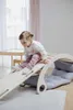 A young child is playing on a wooden climbing structure with a cushion. Produktbild-Vorschau