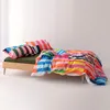 A colorful striped duvet cover and pillow are laid out on a simple wooden bed frame. Voir les images du produit