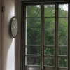 A clock on a wall next to a window with trees outside. Náhled obrázku produktu