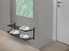 A black metal shoe rack with several pairs of white sneakers on it, mounted on a light gray wall next to a white door. Produktbild-Vorschau