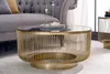 A round coffee table with a gold metal frame and a black glass top is shown in a living room setting. Produktbild-Vorschau
