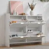 A white shoe cabinet with multiple open compartments and shoes inside, placed against a white wall with a framed picture and a vase of dried flowers on top. Produktbild-Vorschau