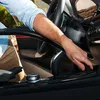 A person is using a vacuum cleaner hose inside a car, cleaning the center console area near the gear shift. Podgląd zdjęcia produktu