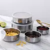 A set of stainless steel food containers with clear lids, some filled with pasta, coffee beans, and red beans, arranged on a marble-like surface with lime slices and cutlery in the background. Produktbild-Vorschau