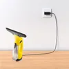 A yellow window vacuum cleaner is placed on a wooden table, with its charging cable plugged into a wall socket. Produktbild-Vorschau