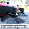 Close-up of the brushes of a red and black sweeping machine on a paved surface. Produktbild-Vorschau
