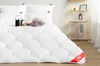 A white duvet with a scalloped pattern is laid out on a bed, with pillows behind it. A small black teapot and a bouquet of dried flowers are placed on the duvet. Produktbild-Vorschau