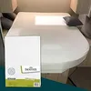 A white fitted sheet is shown on a bed, likely in a campervan or caravan, with a packaging box in the foreground. Produktbild-Vorschau