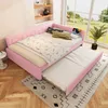 A pink daybed with a pull-out trundle bed is set up in a room with a large window overlooking a garden. Pillows and blankets are arranged on the daybed. Podgląd zdjęcia produktu